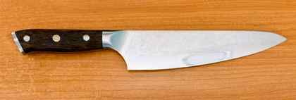 Chef knife with a Damascus-pattern blade and dark timber handle, laid flat on a timber bench