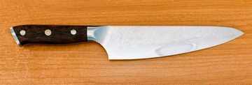 Chef knife with a 200 mm blade laid flat on a timber bench, showing blade length measured from heel to tip